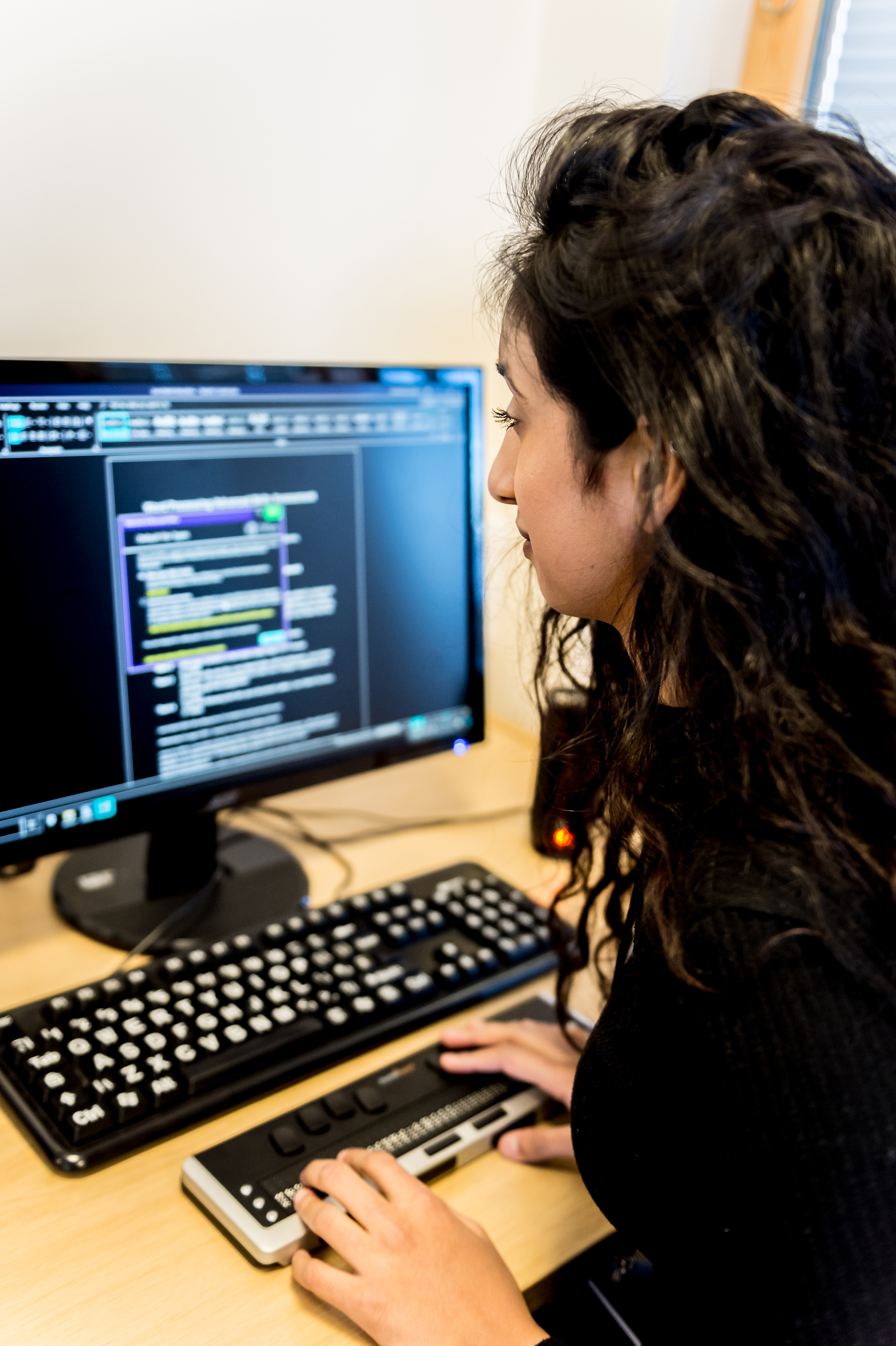 a female student sits in front of a computer screen using assistive technology