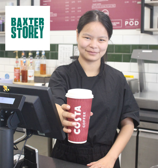 Guoguo stands behind the cafe counter holding out a coffee cup to a customer who isn't in shot