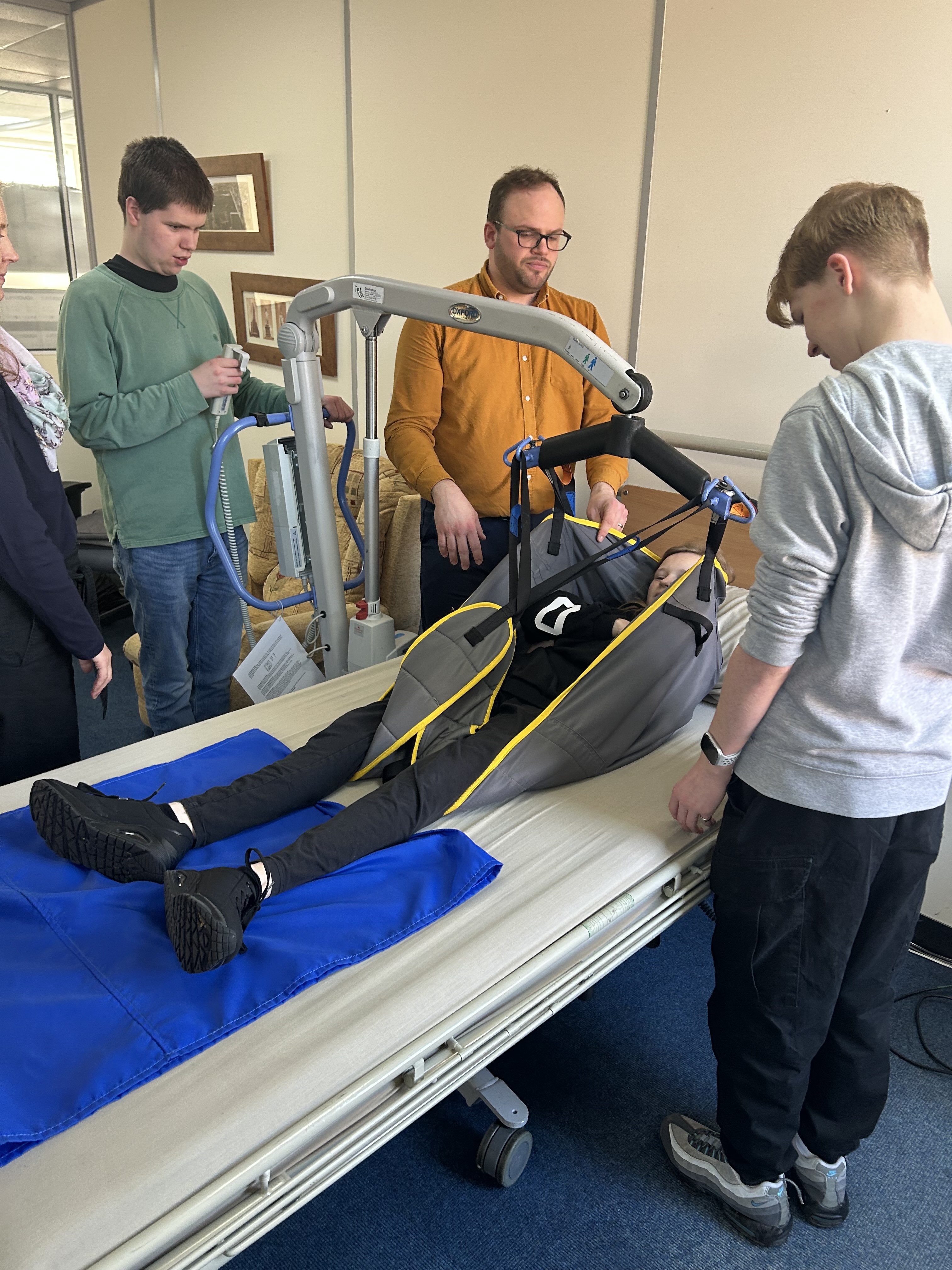 a student being hoisted on to a bed by a professional as two students look