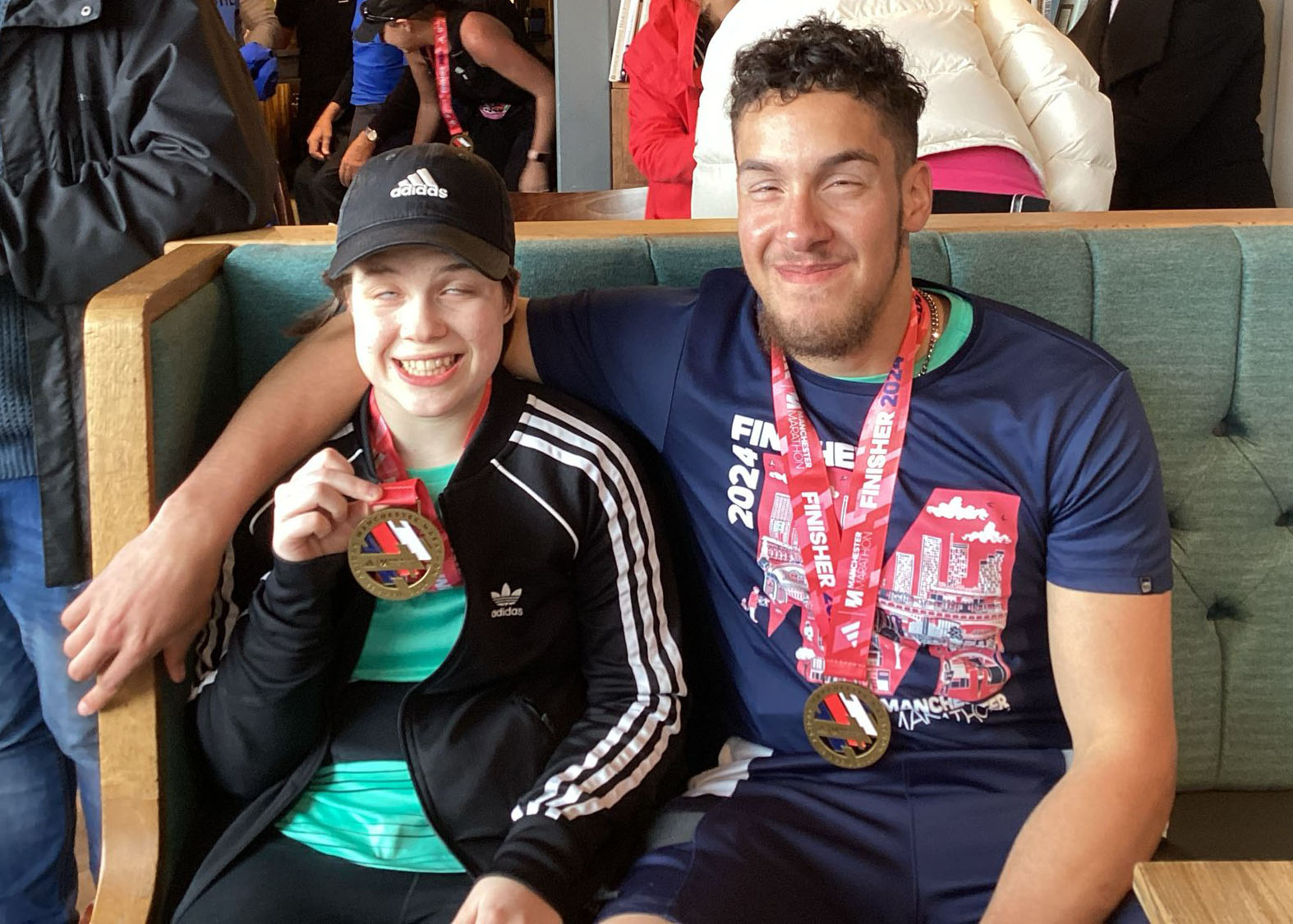 sitting next to each other both with beaming smiles and holding up their medals