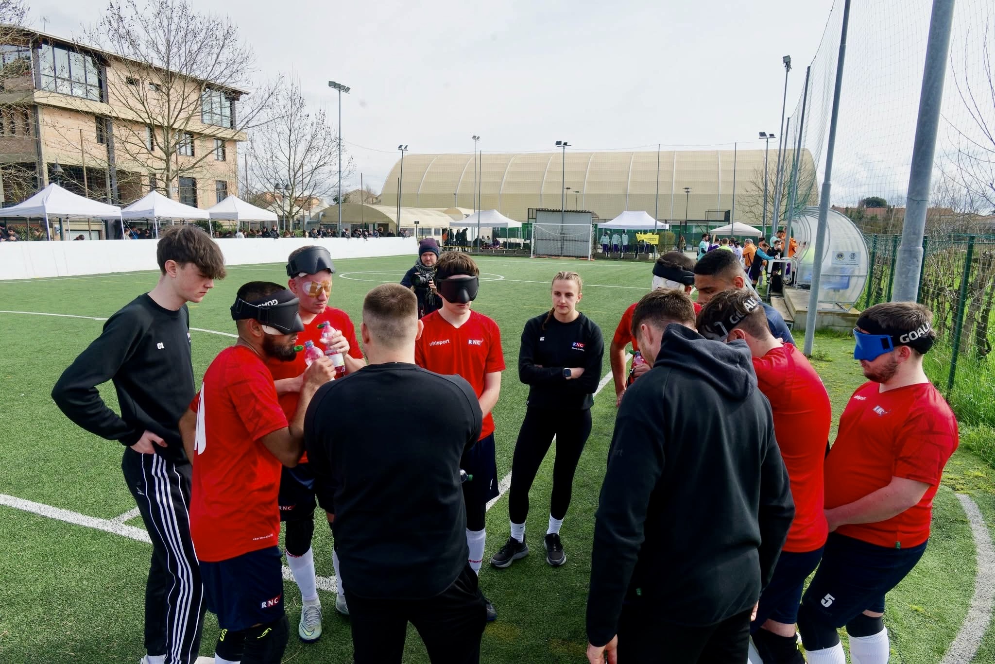 the team on the pitch in a huddle talking. They are wearing red shirts and navy shorts