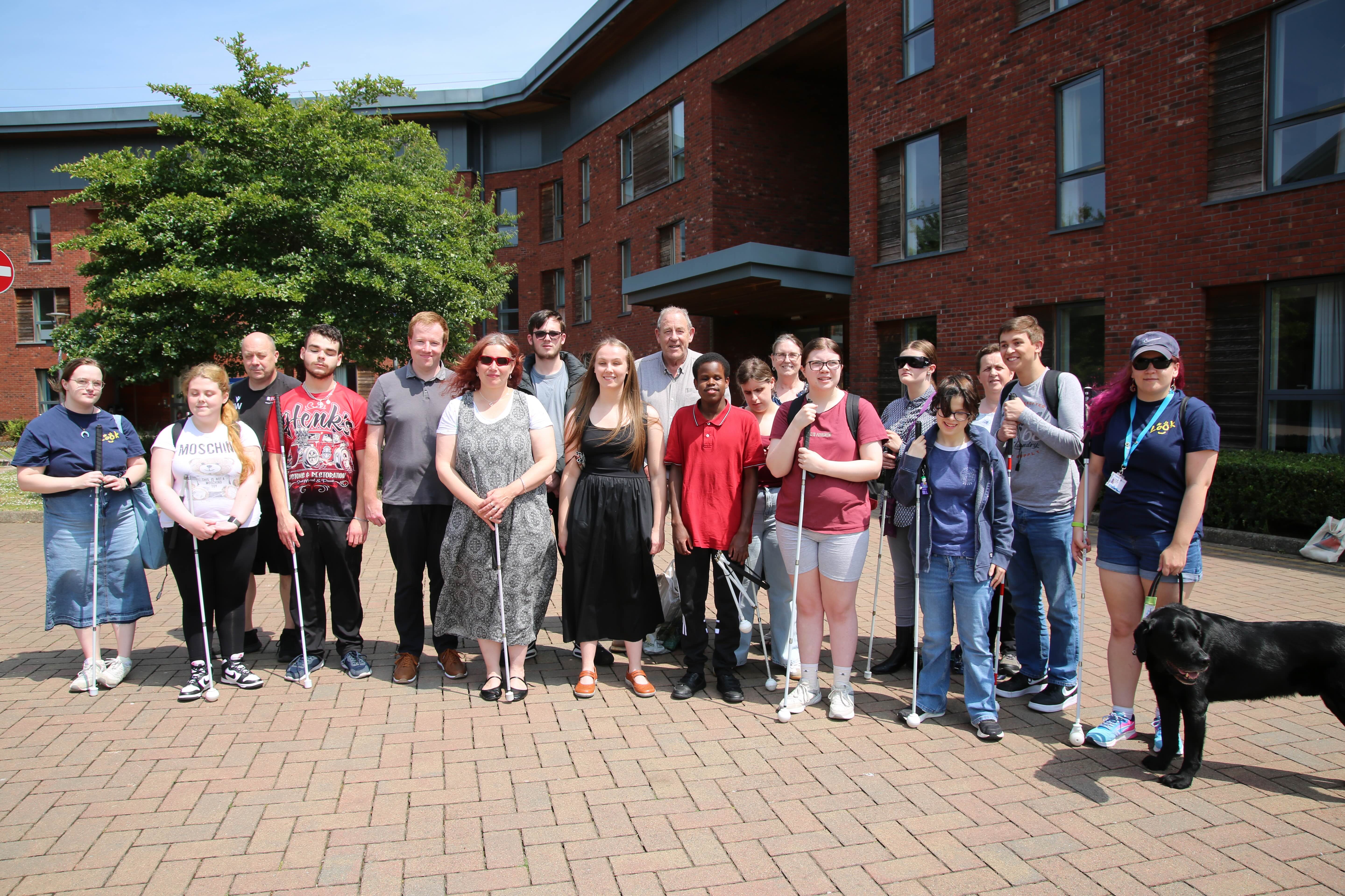 A group of people standing in a courtyard of the university campus smiling in the sunshine