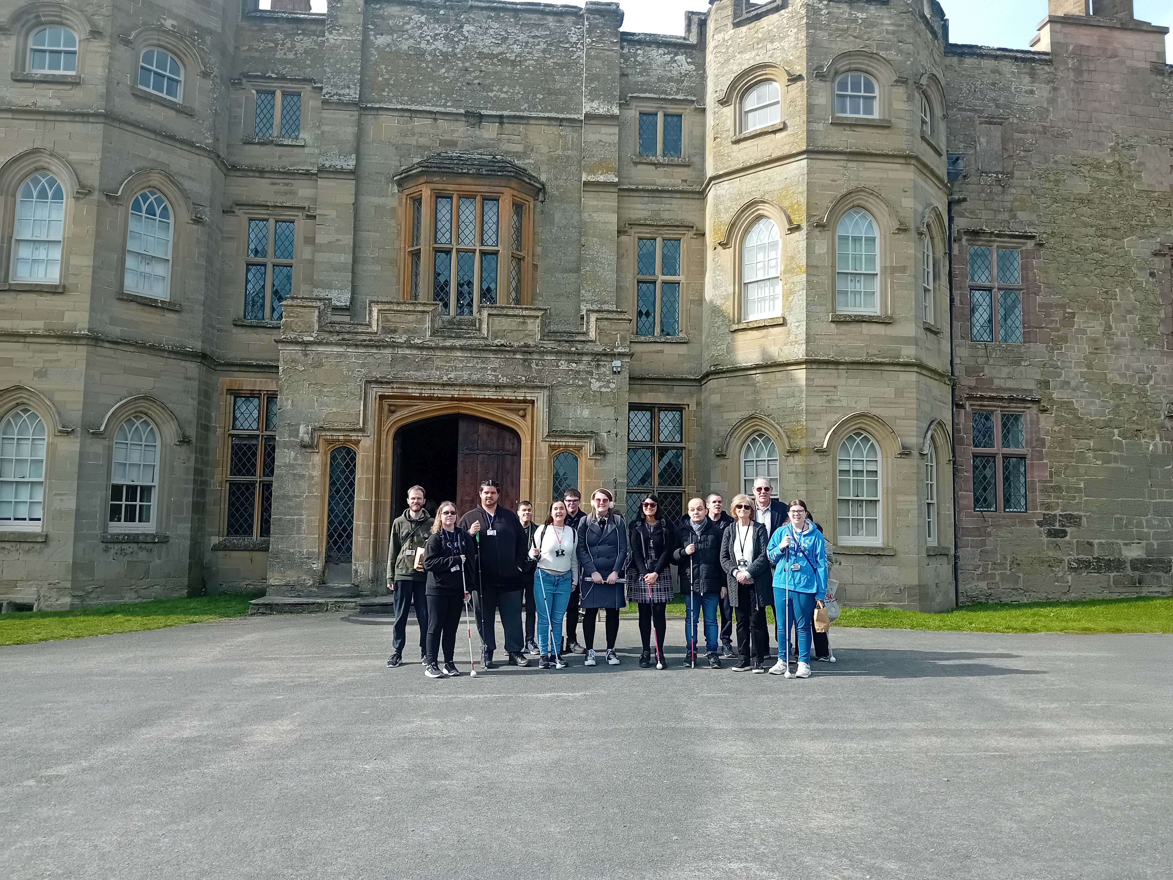 A group of people standing outside in front of a large historic stone castle.