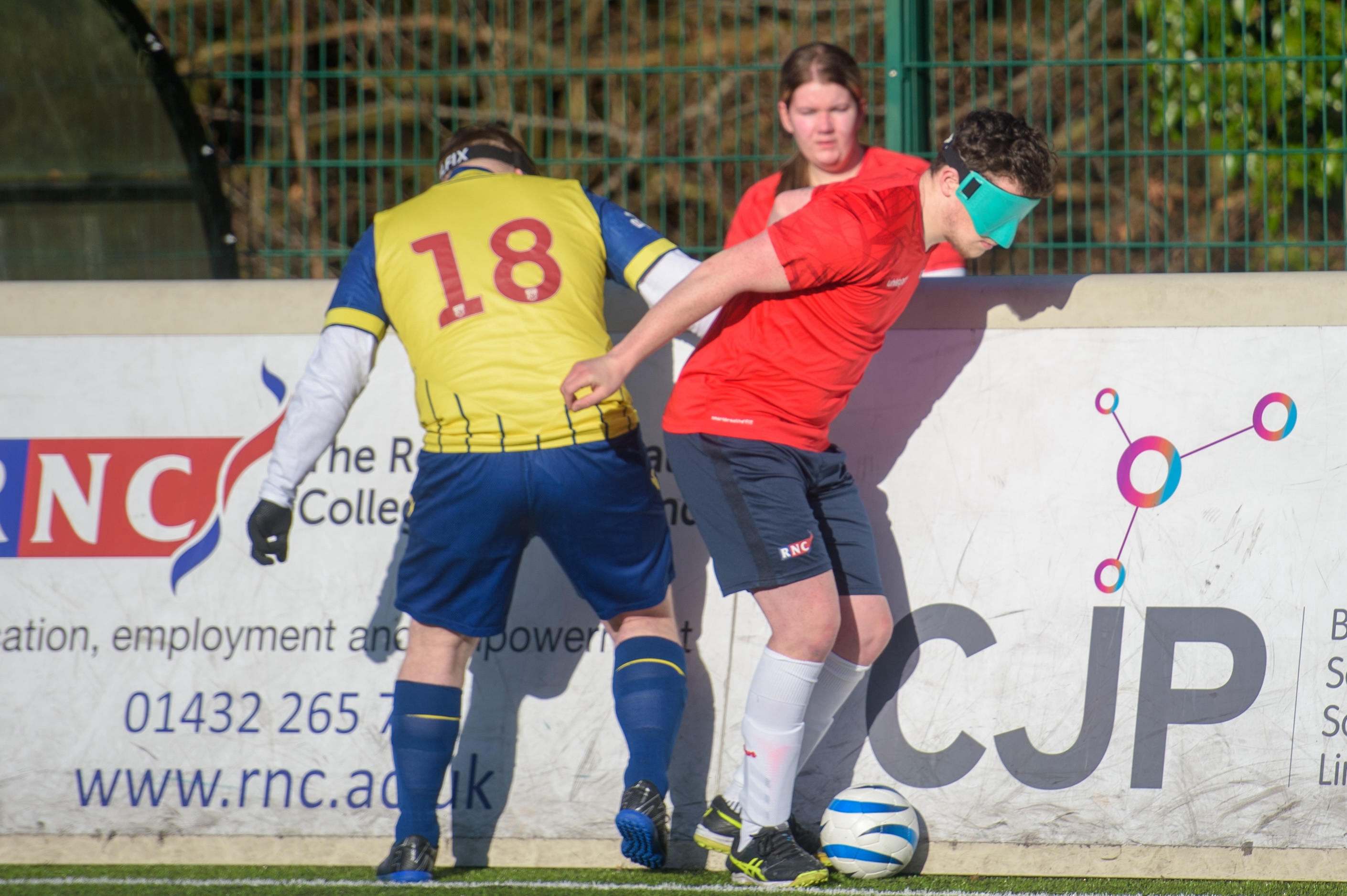 An RNC player in red shirt blue shorts against the boards, on the ball as a WBA player tries to pull him back