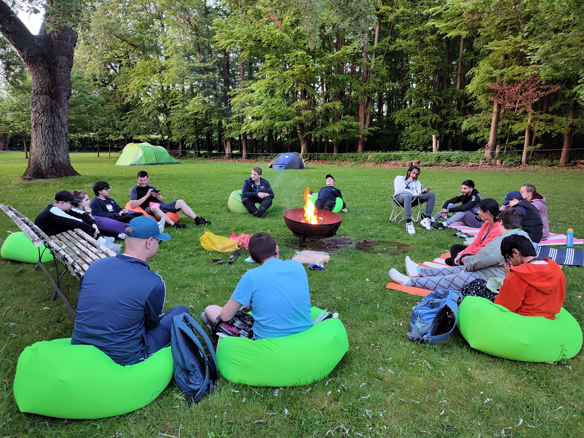 students sitting around the campfire with their tents in the background