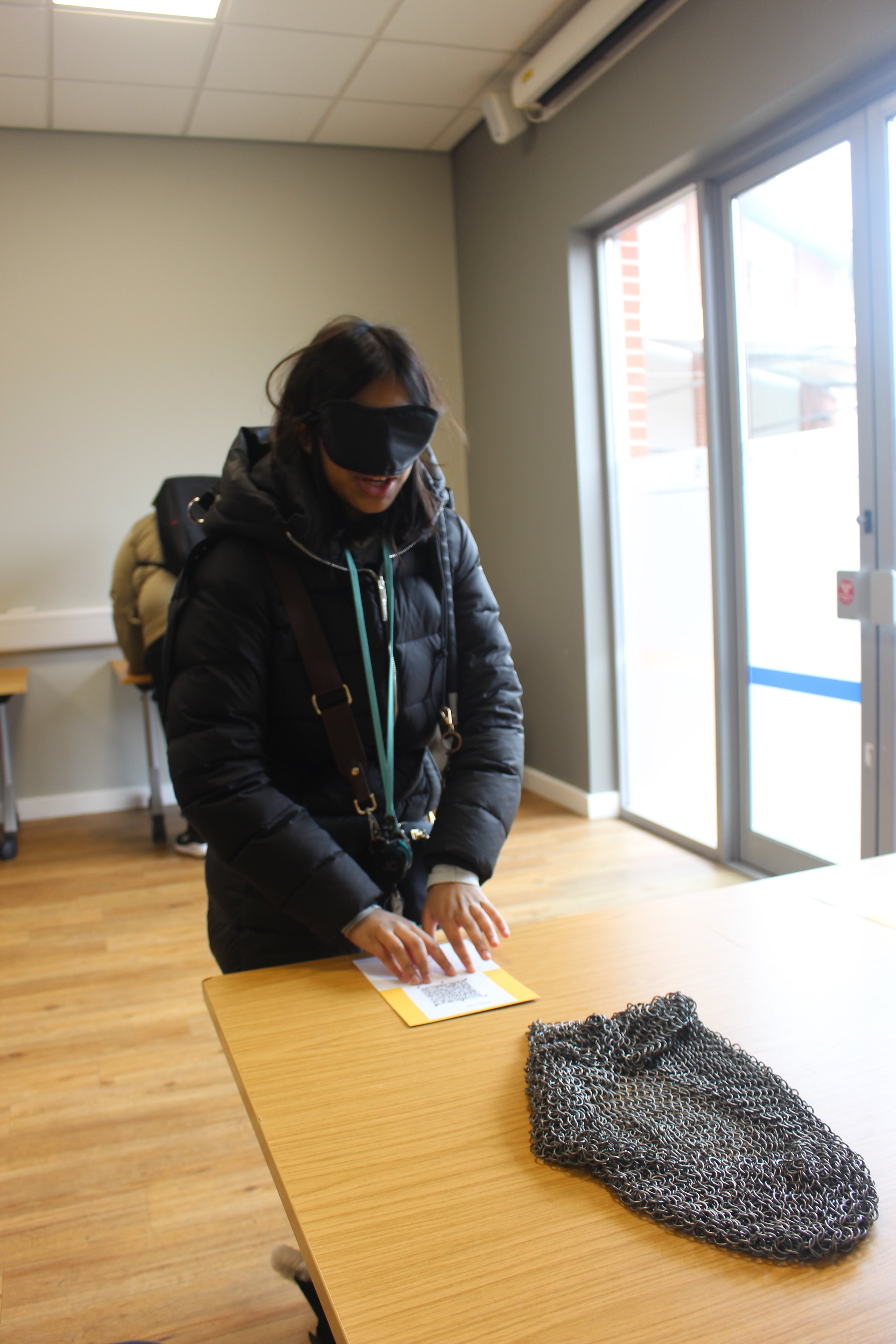 A blindfolded visitor reading the braille description of a chainmail headdress