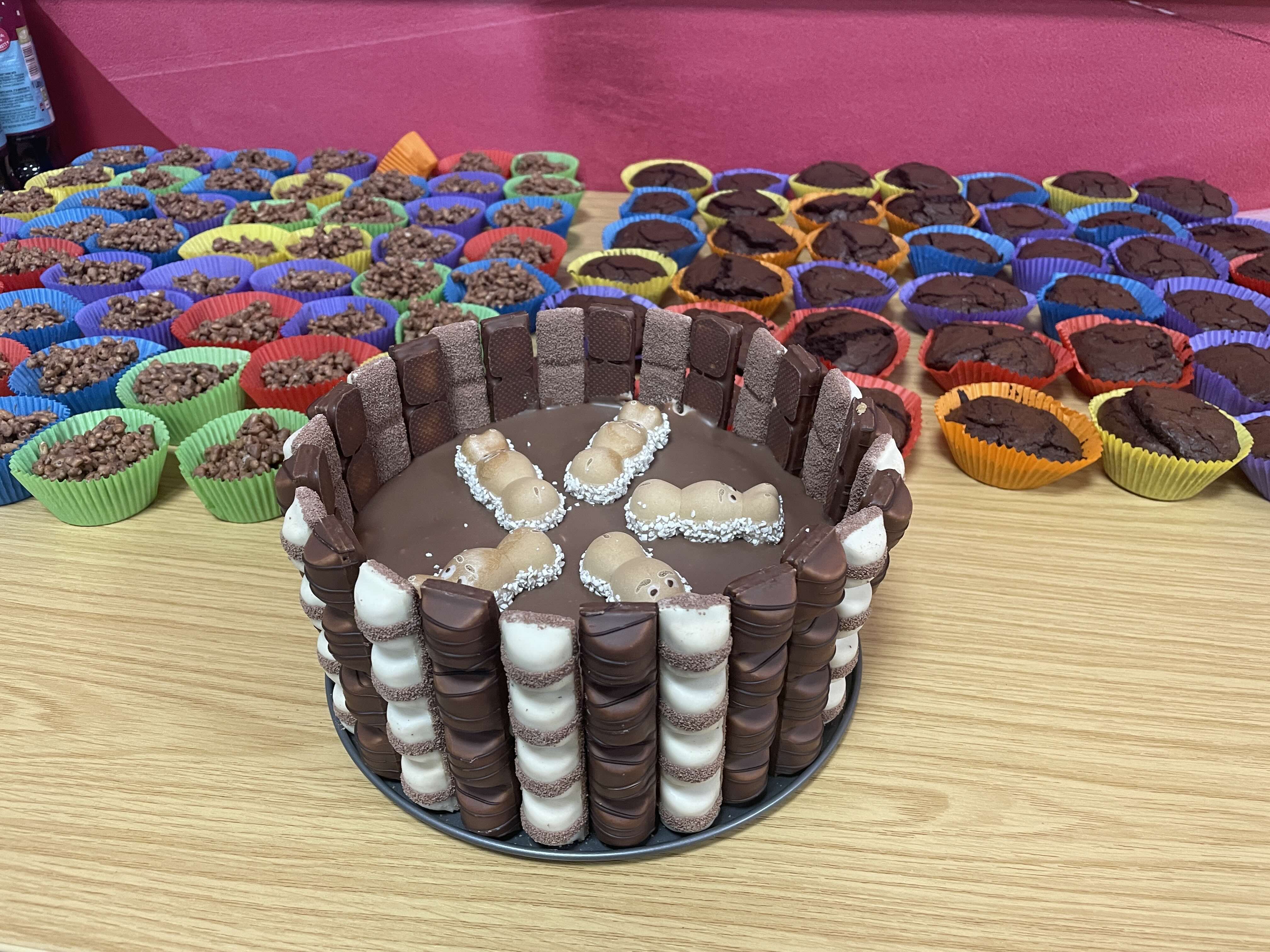 a chocolate cake surrounded by lots of rice crispy cakes and chocolate cupcakes in brightly coloured cake cases