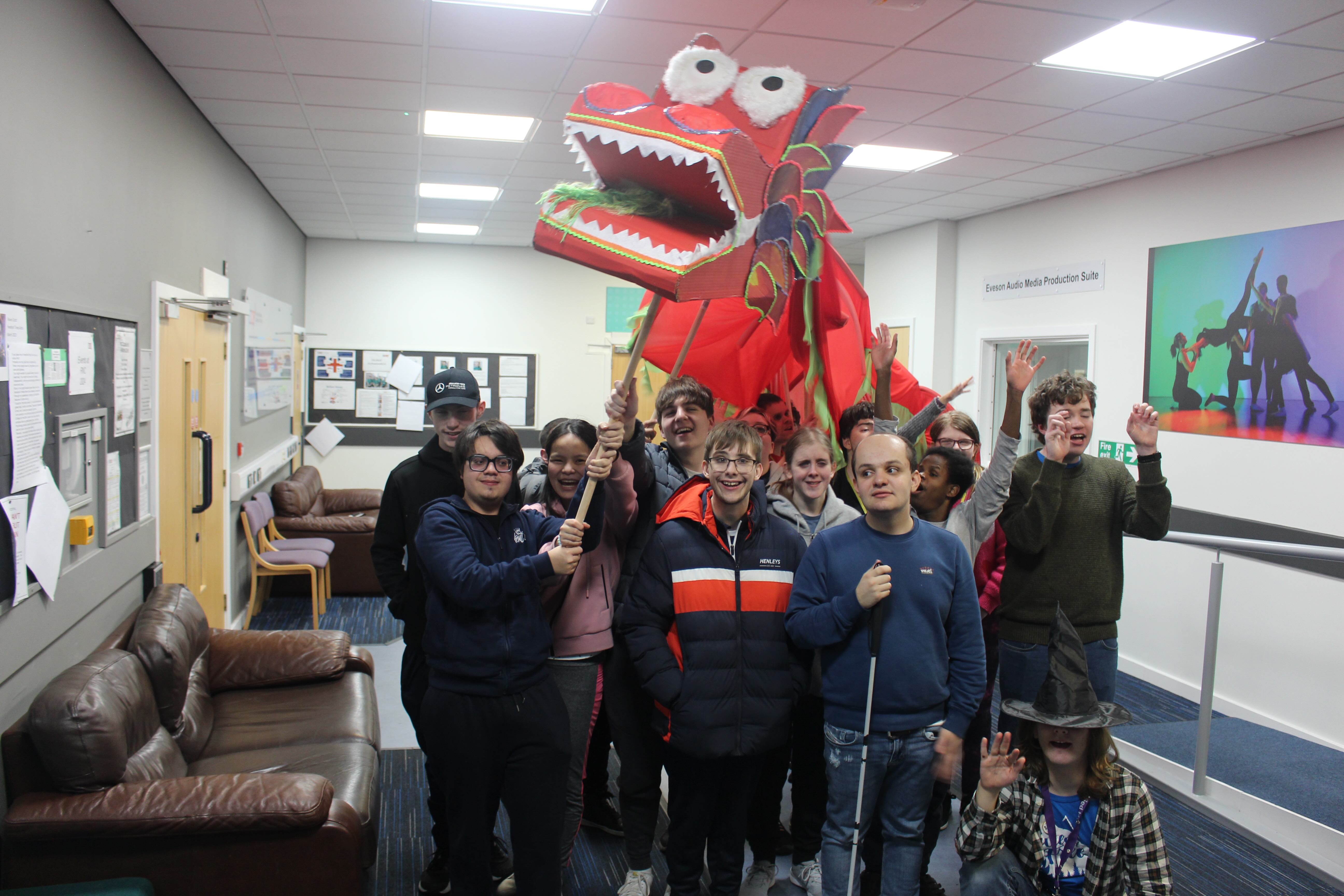 The bright red dragon head with a large group of students cheering around it