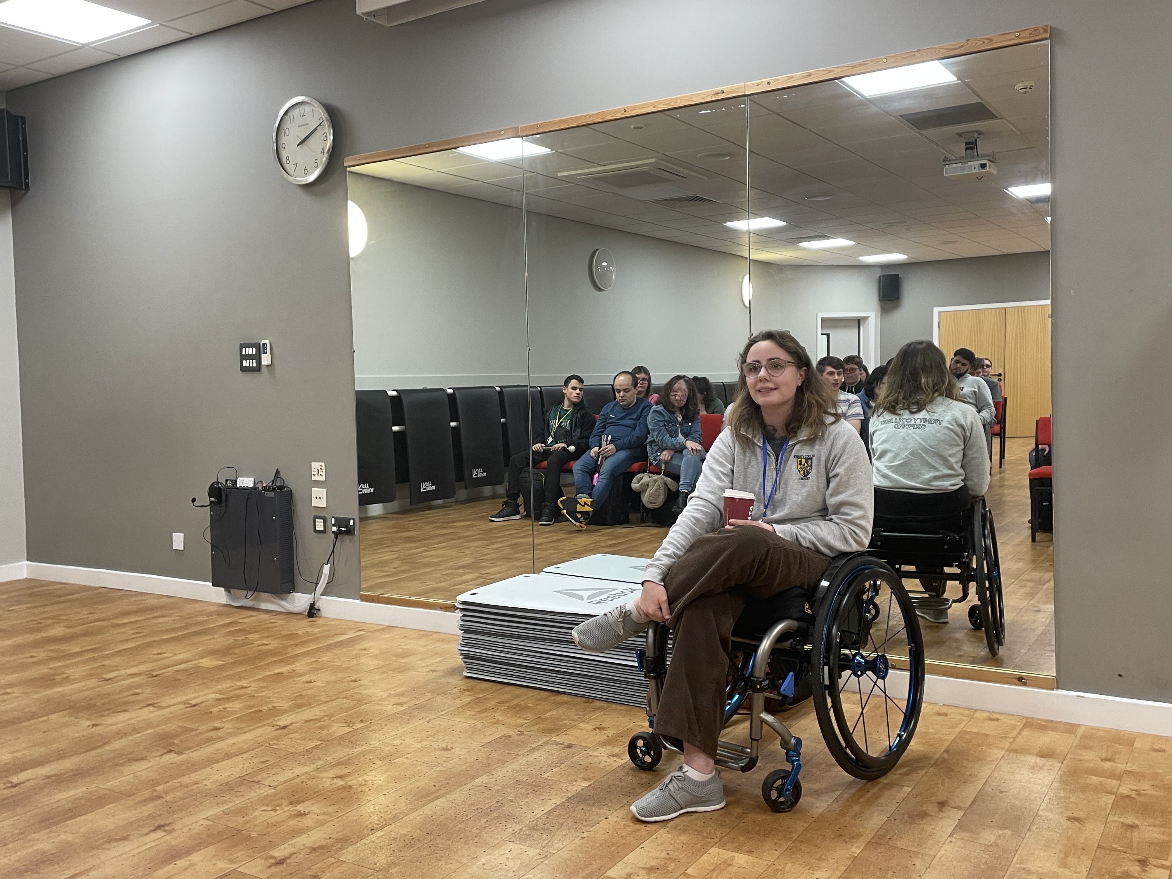 In the dance studio with a wall mirror - Tiri sits in front of the mirror facing the audience in a wheelchair and the audience can be seen in the mirror behind her