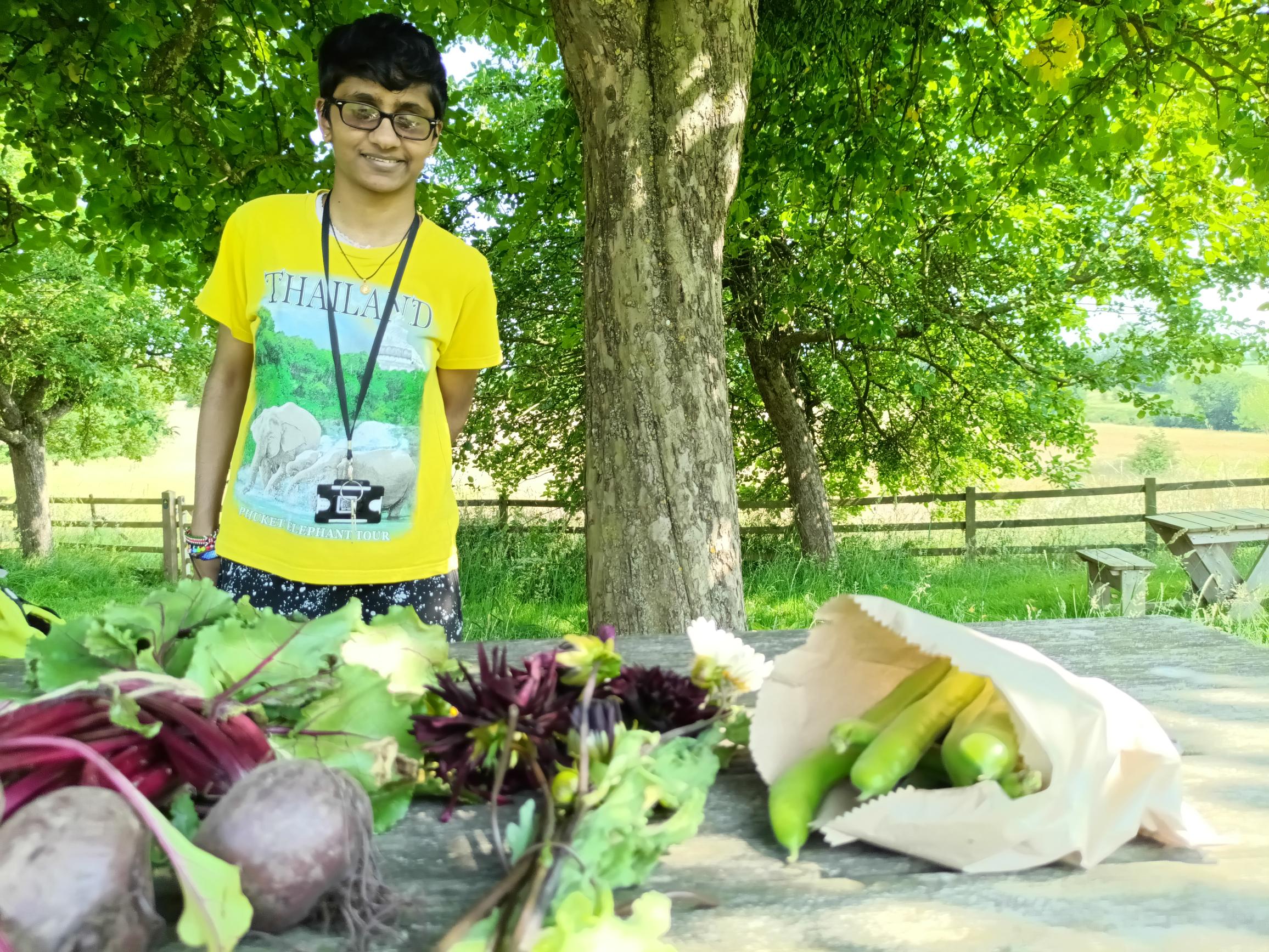 Sonali standing behind a table which is laden with brown paper bags full of various vegetables grown in the walled garden