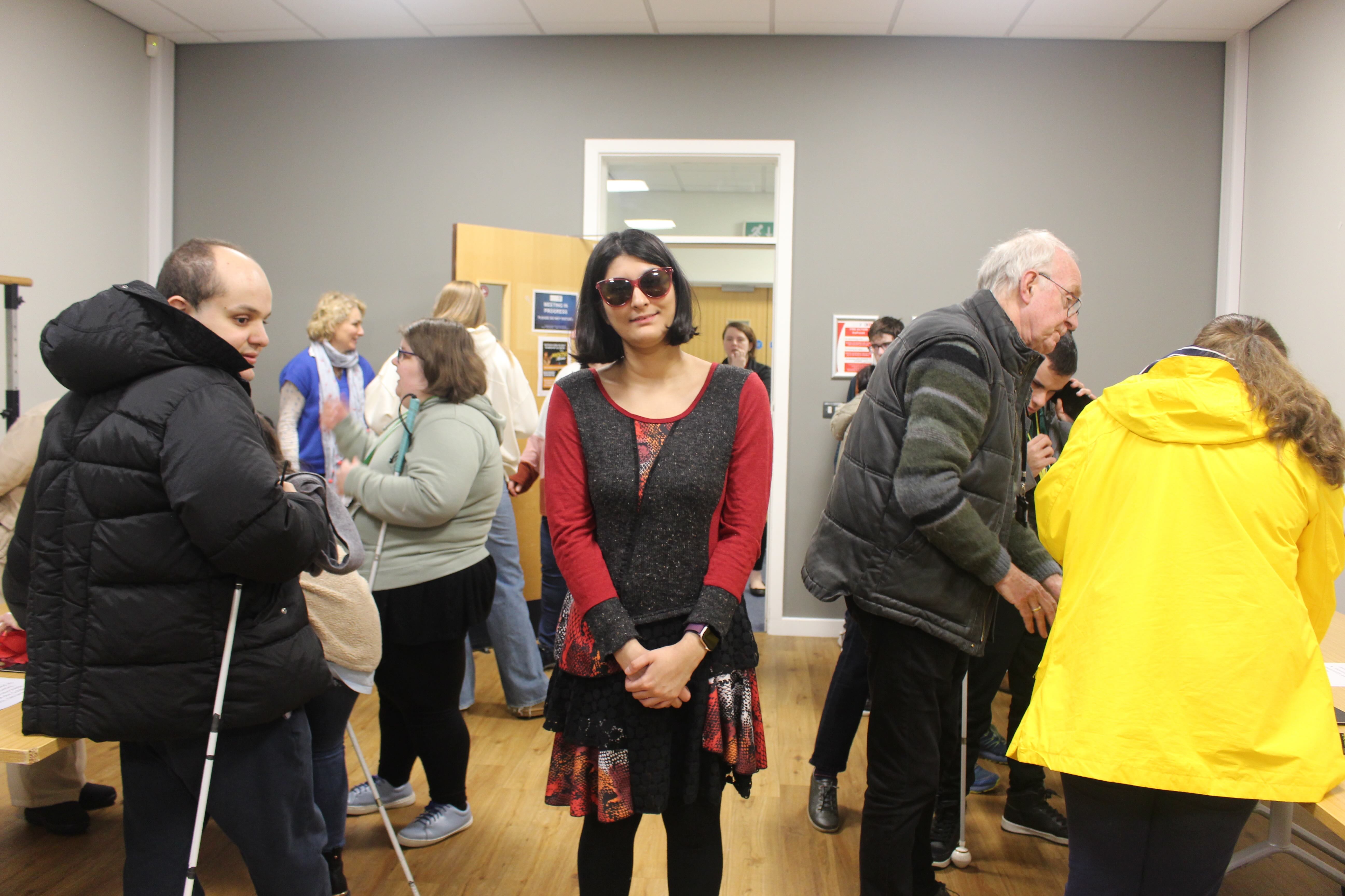 Maleeka stands in the centre of the room with the exhibition going on around her