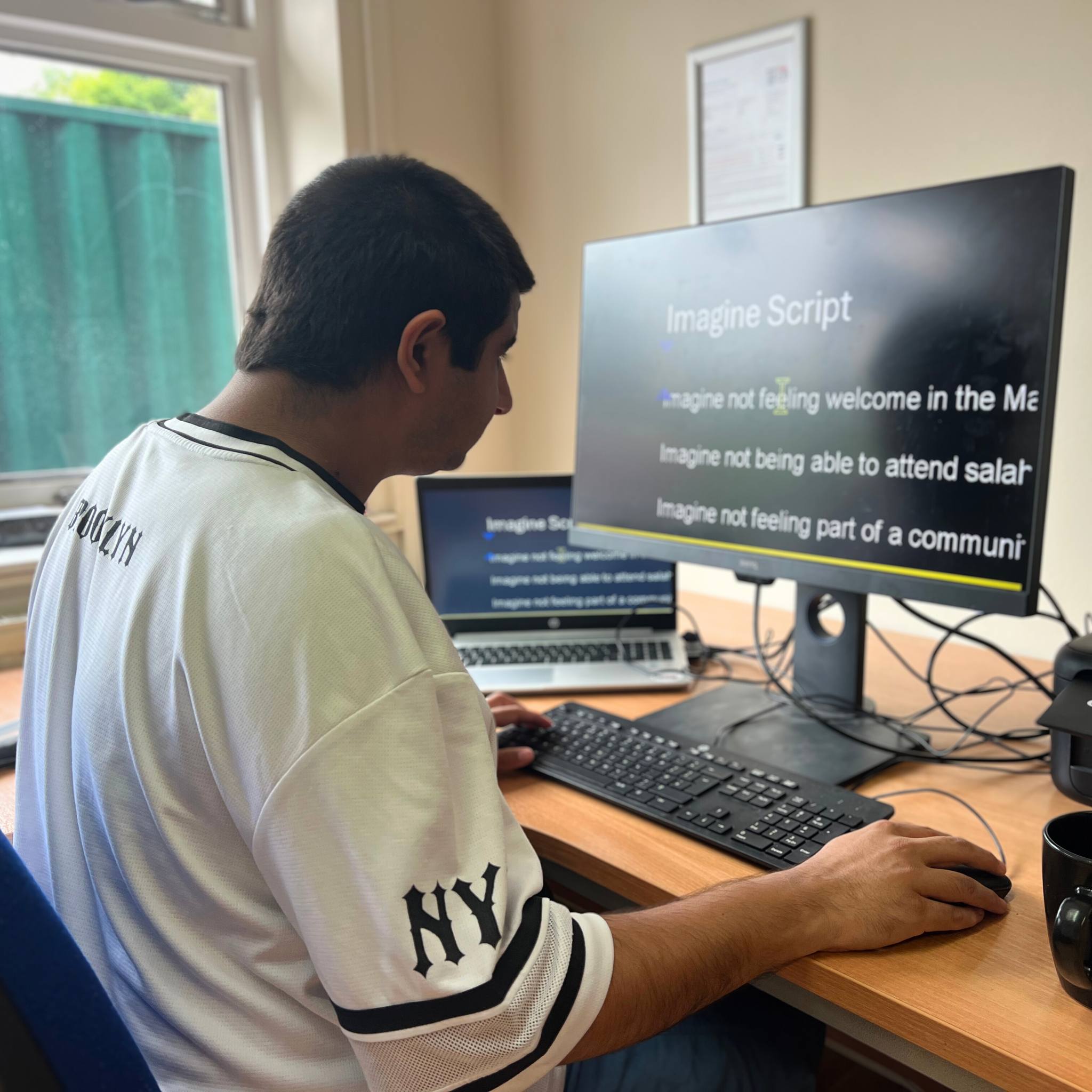 A student sits at a desk in front of a computer screen with the words zoomed in on 'imagine script'