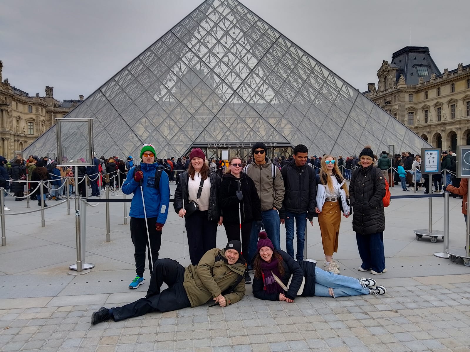 The group of students and staff in front of the glass pyramid entrance to the Louvre Museum