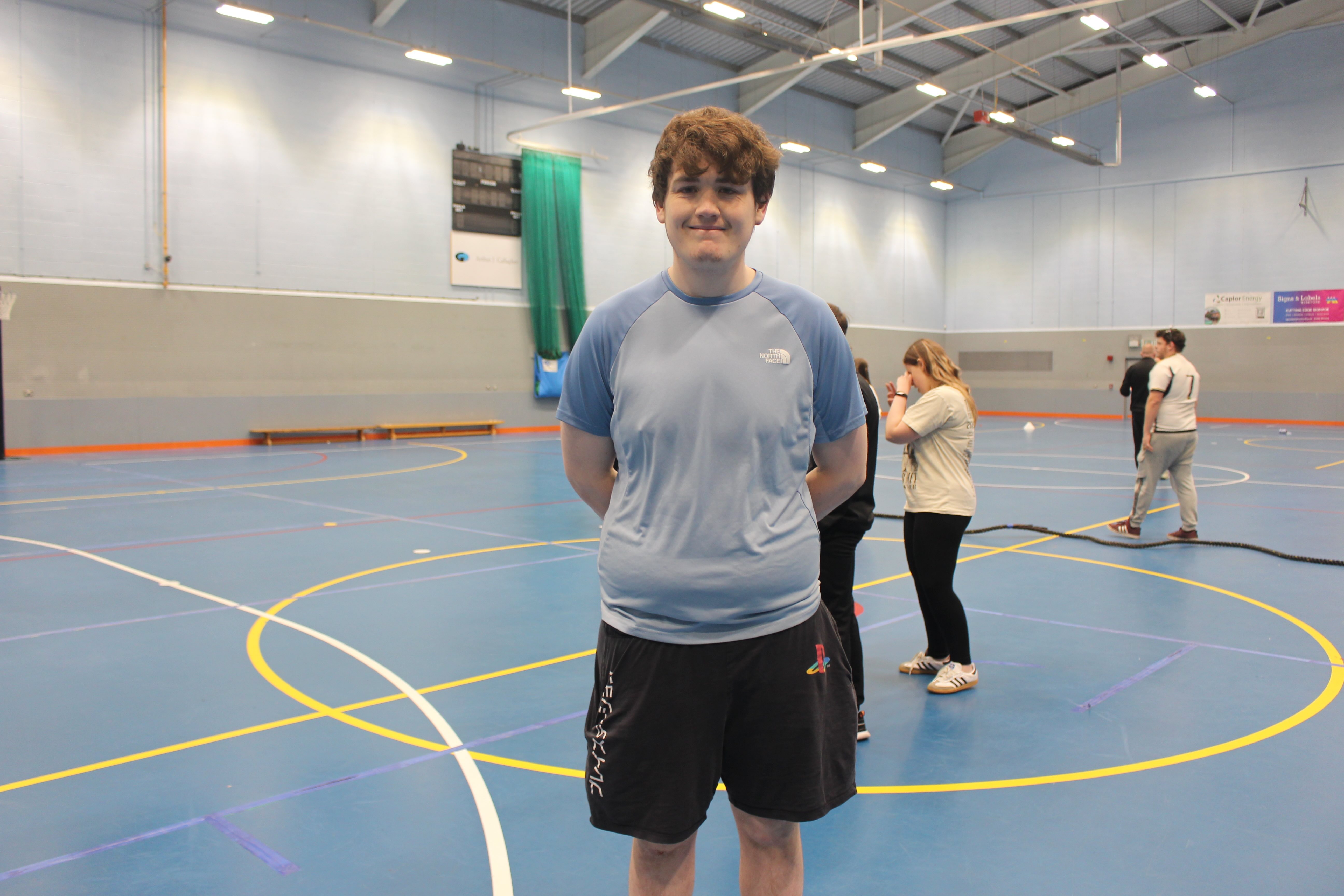 young man standing in the sports hall. There are a few people behind him