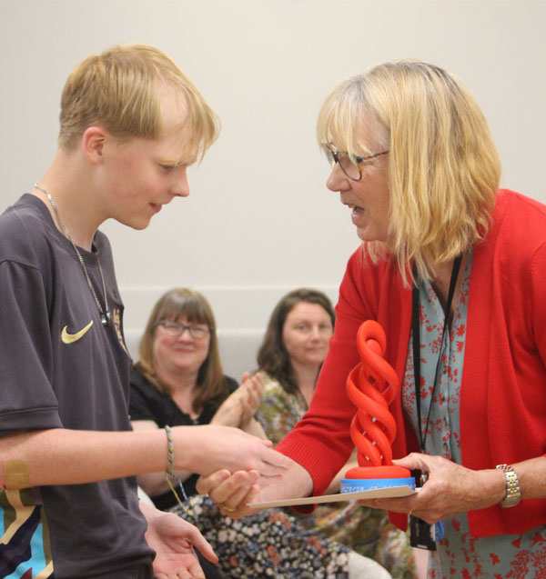 A student shakes hands with a member of staff before receiving his award and certificate