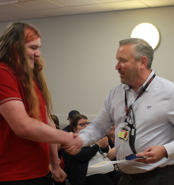 A student shakes hands with a member of staff while collecting his award