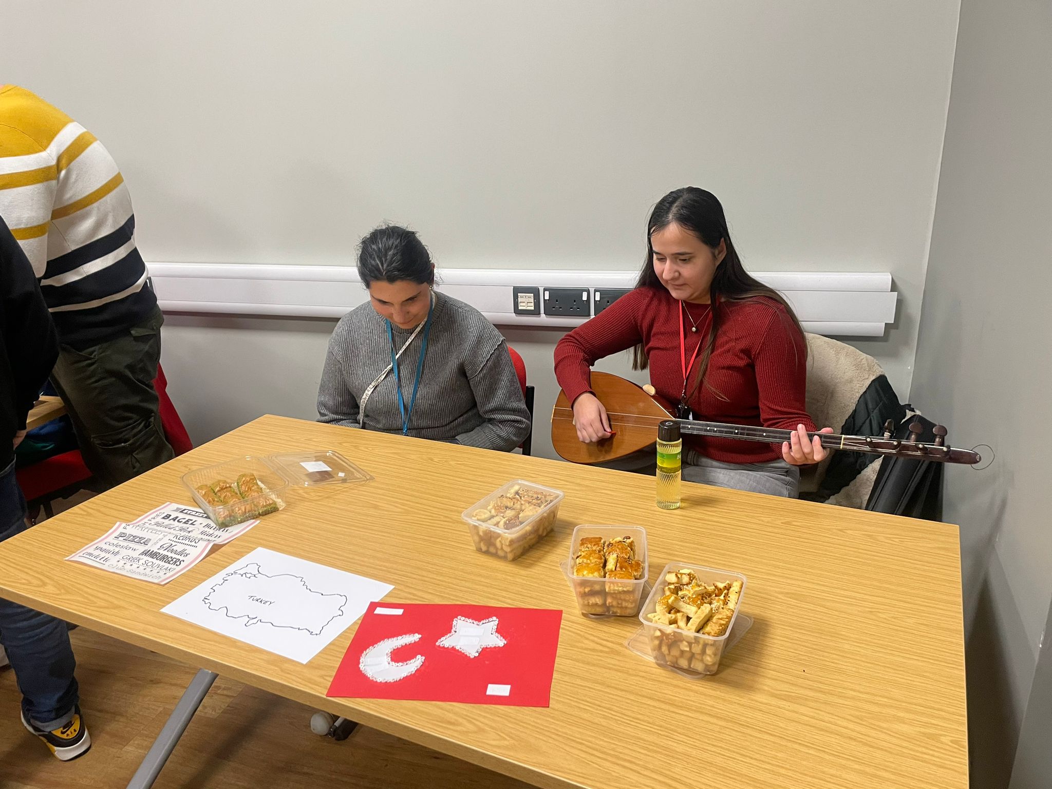 two students sitting at the Turkish table one is playing the saz