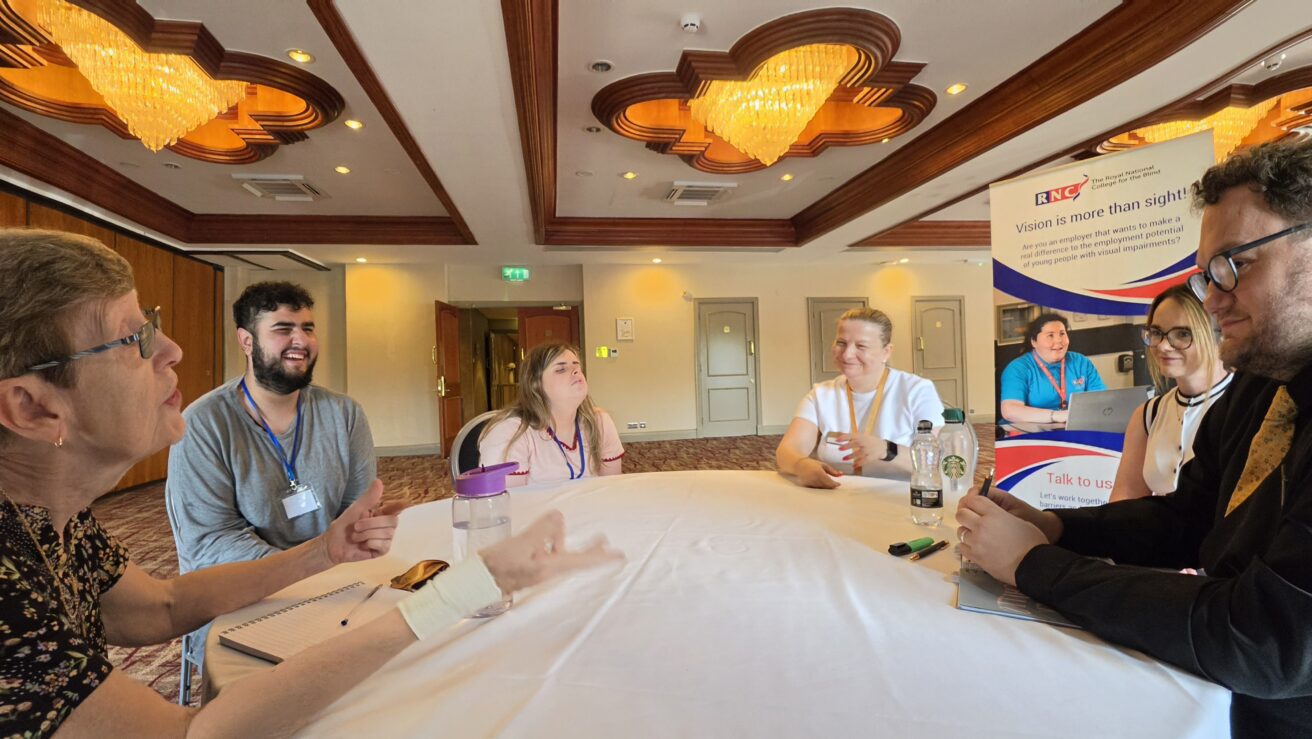 A group of people sitting at a circular table chatting and smiling.