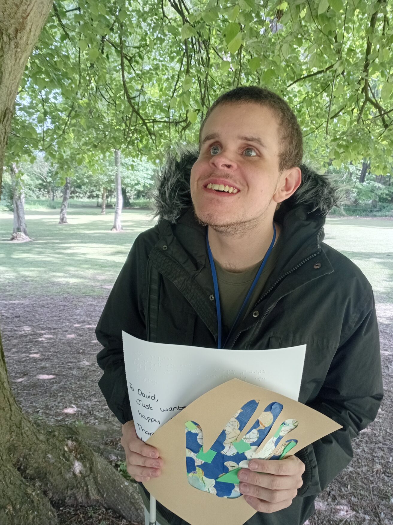 Matteo standing under a tree in the orchard smiling and holding up his handcrafted card