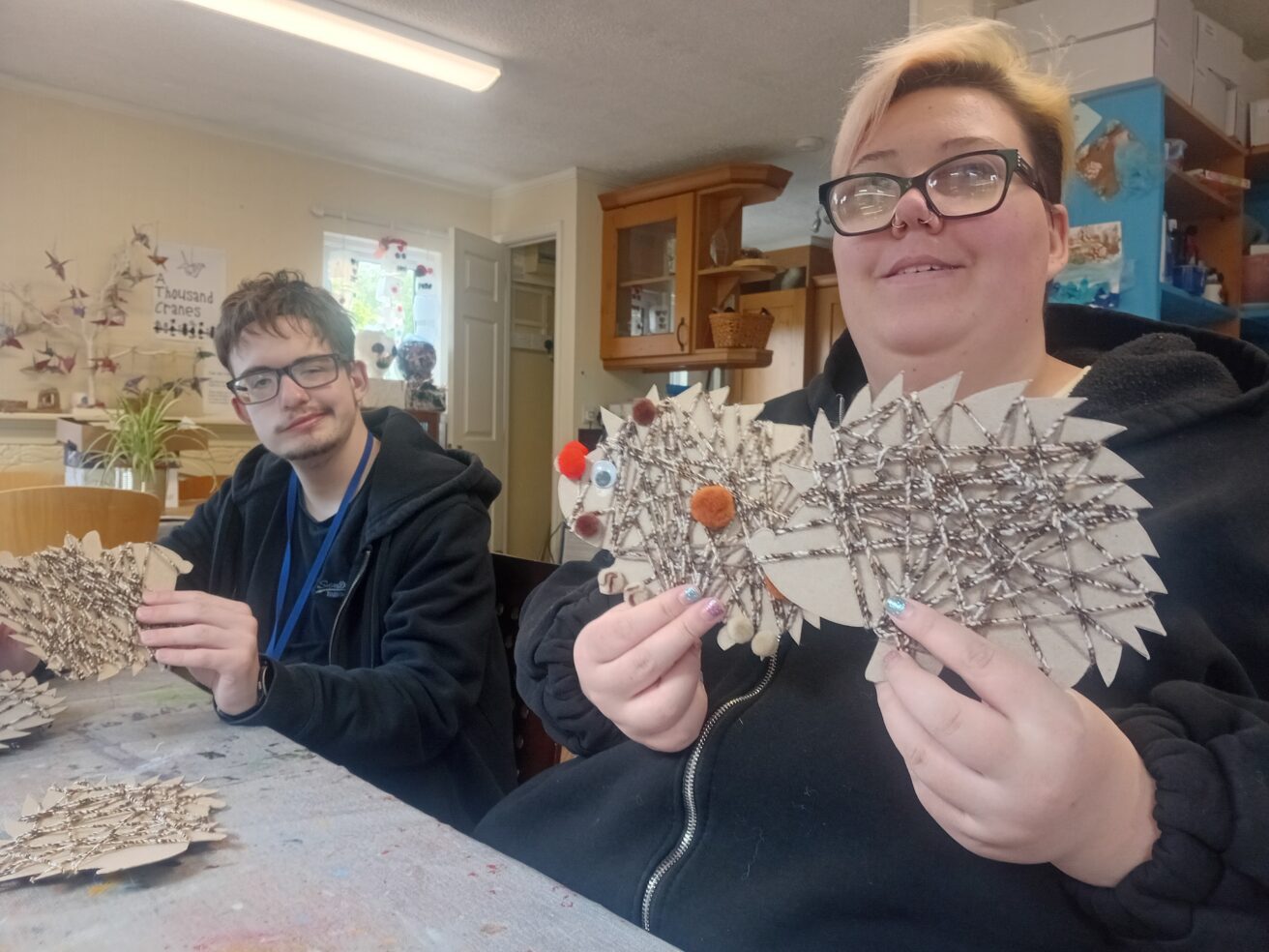 Jacob and Molls hold up their 2D hedgehogs - made from cardboard, twine, stick on wobbly eyes and fluffy noses
