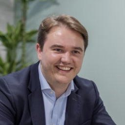 A head and shoulders profile picture of Chris wearing a blue suit and shirt