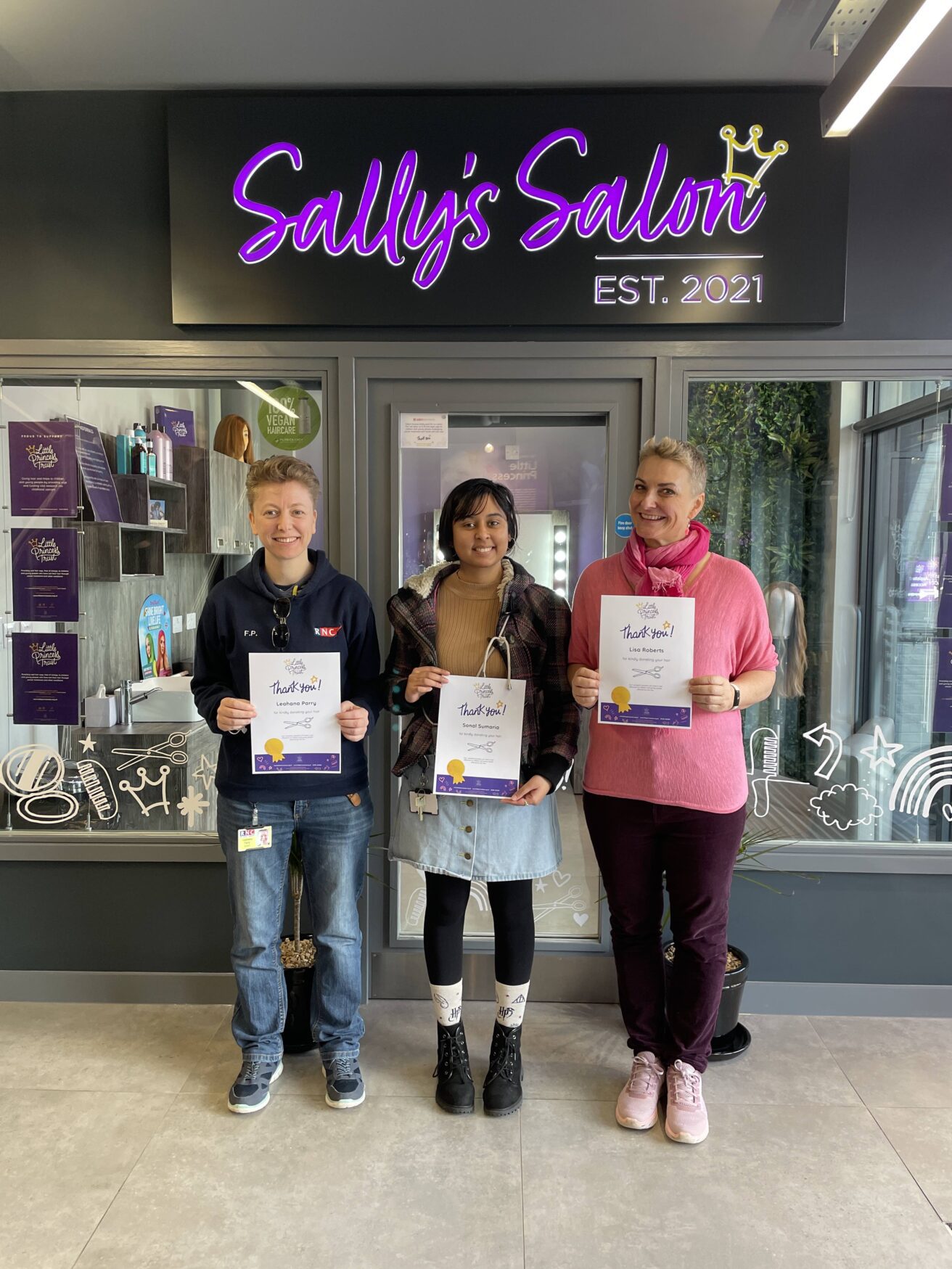 Flea, Sonal and Lisa stand in front of Sally's Salon holding up their certificates