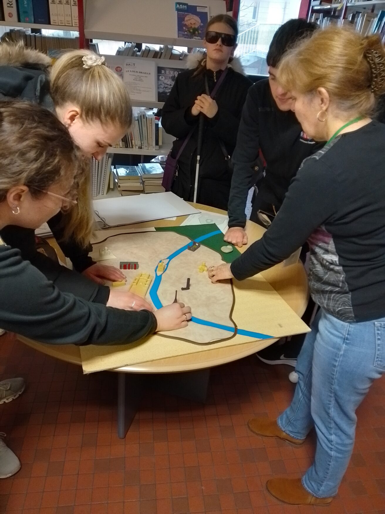Students group around a table with members of the University's Braille Transcription Team and explore a tactiel map of Paris