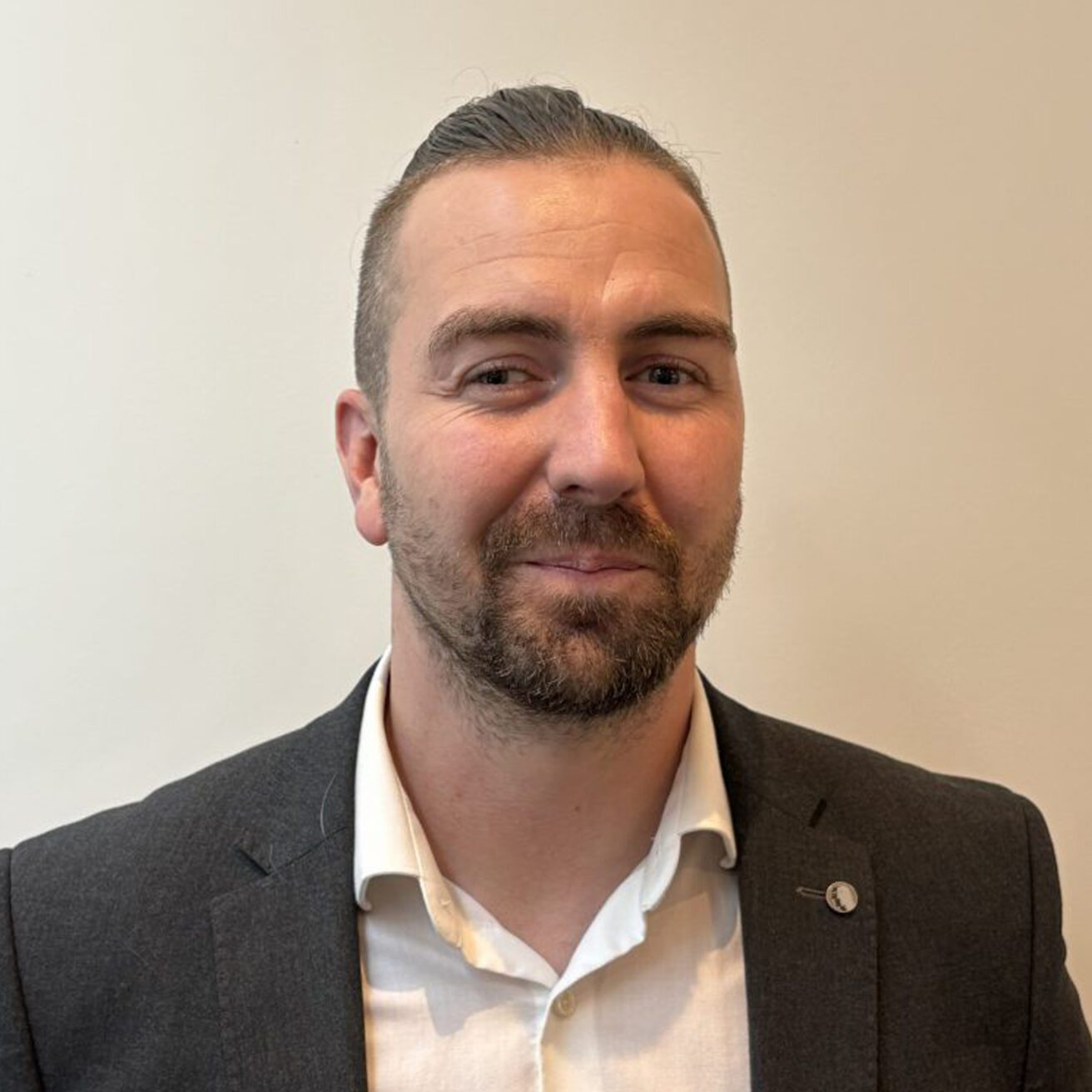 Photo of Josh - he has brown hair, a short beard and moustache and is wearing a gray blazer and shirt