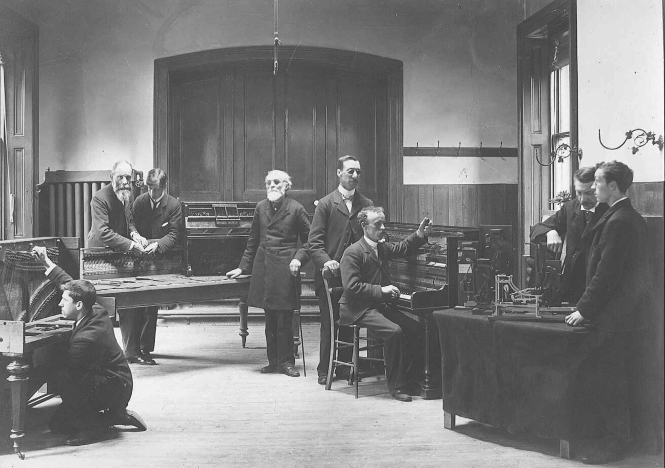 A picture from the 1800s showing male students being taught piano tuning