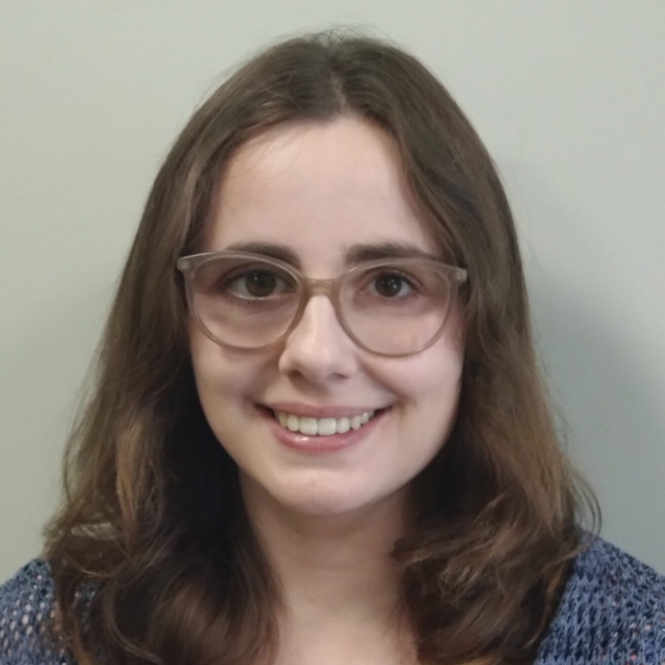 A head and shoulders picture of a Tiri with long brown hair wearing glasses