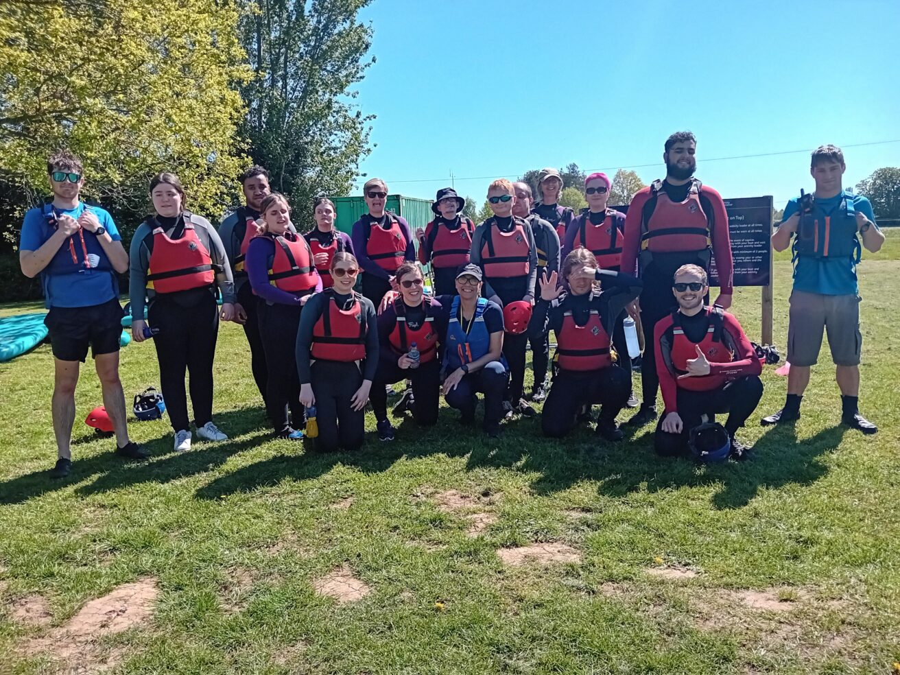 the group of centre staff with RNC students, staff, and volunteers all wearing buoyancy aids - standing on grass with a bright blue sunny sky above
