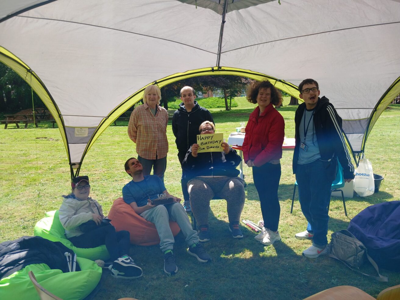 the group singing happy birthday - some sitting, some standing under an gazebo in the orchard