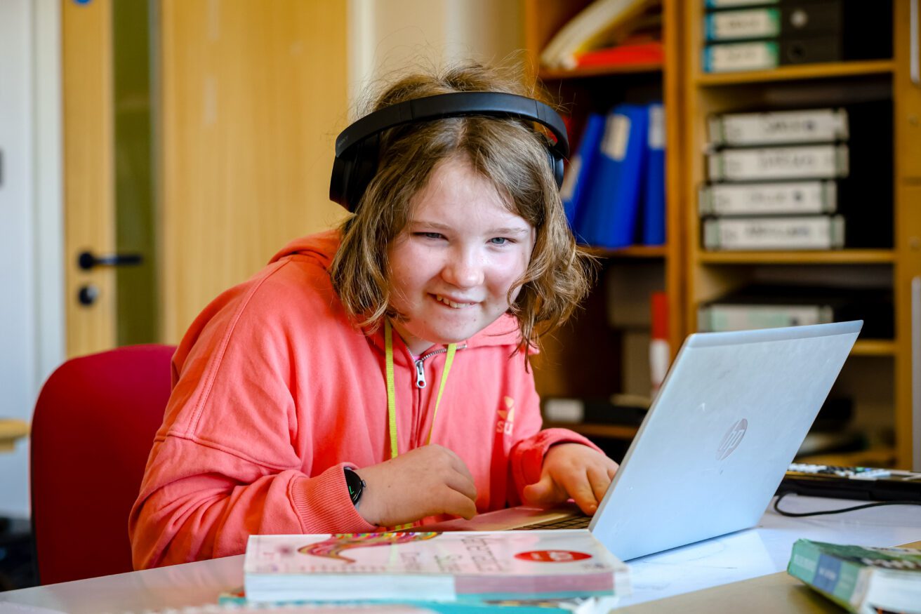 A student wearing headphones and working on a laptop in front of her in a maths class - there are some books in the foreground
