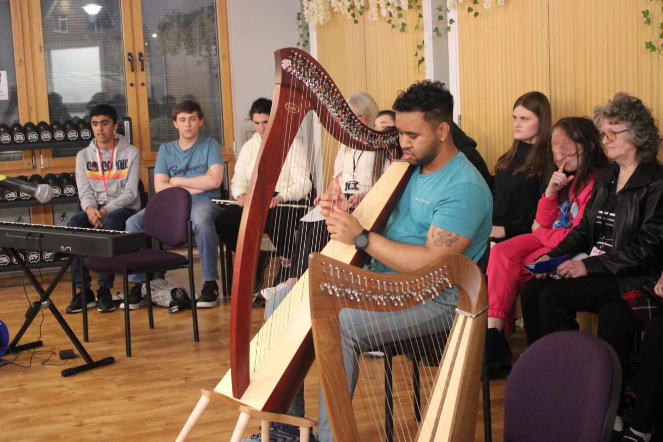 A student showcasing his harp playing at a celebration - other student performers are sitting behind him