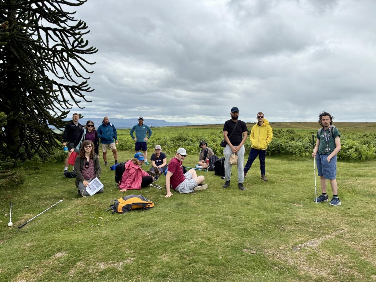 A group of students wearing walking clothes and boots sitting and stading at the top of a hill