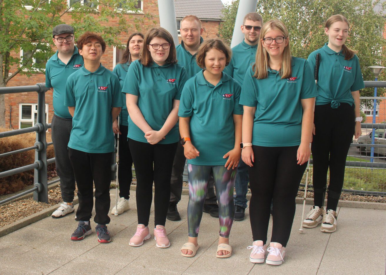 The full group of 9 ambassadors wearing their green polo shirts all standing and smiling