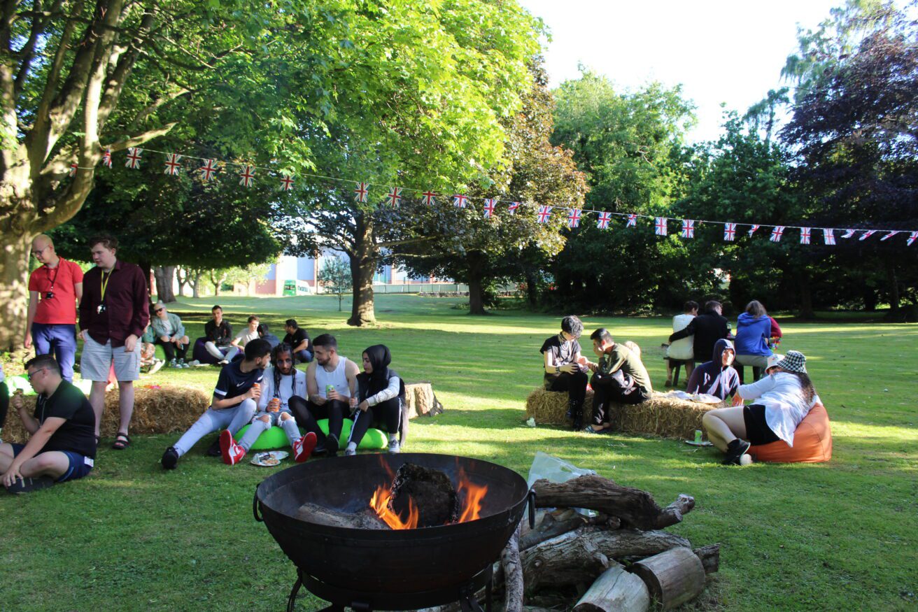 students relaxing in the orchard on beanbags and there is a lit firepit in the foreground of the picture