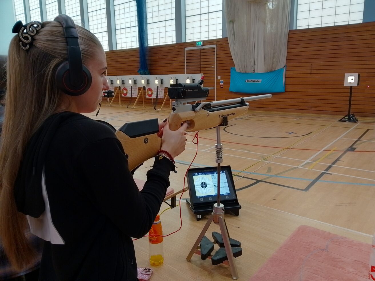 Tegan wearing headphones with her finger on the trigger of her rifle looking towards the target