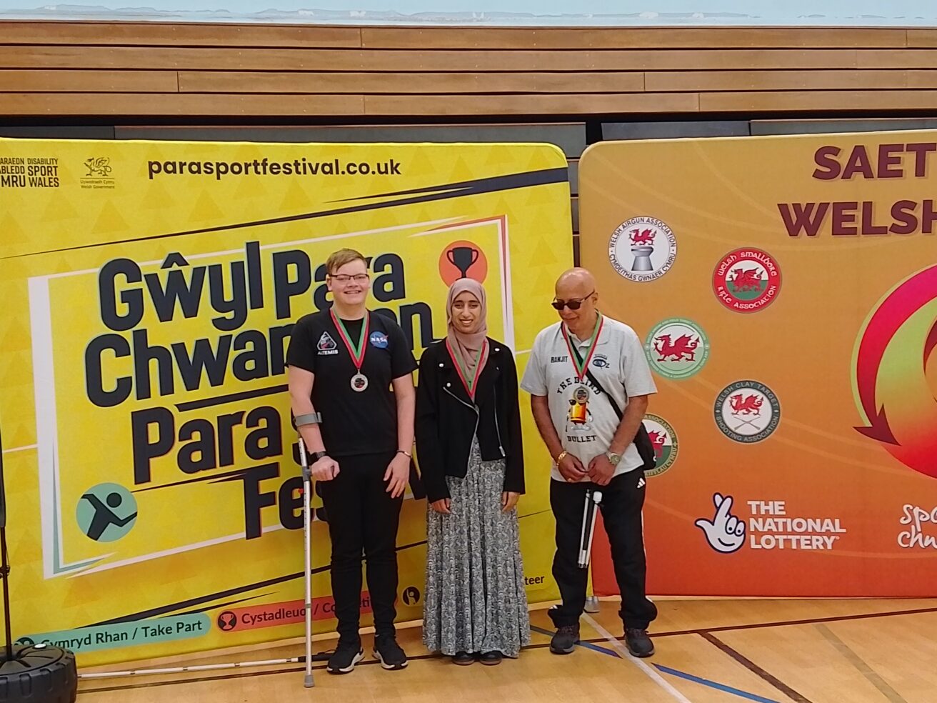Harvey and Humna standing in front of colourful competition publicty with another male medal winner