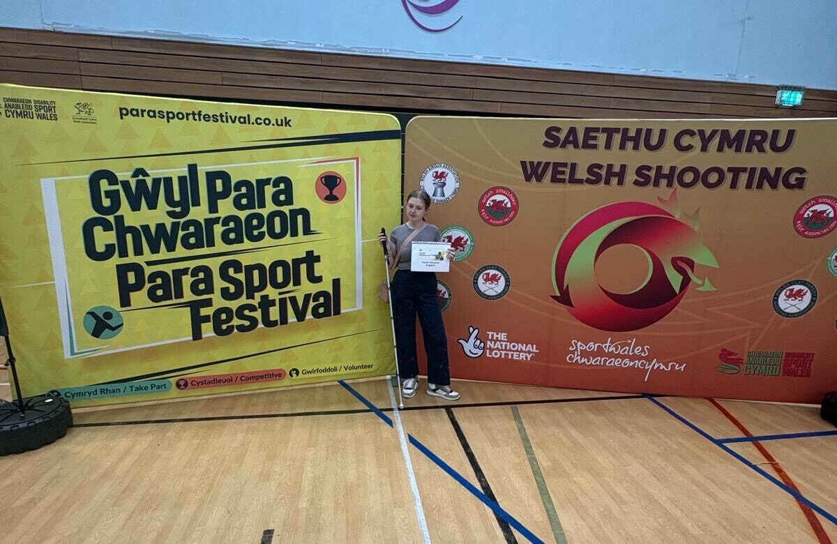Dayzie stands with her cane and certificate in front of the competition publicity boards