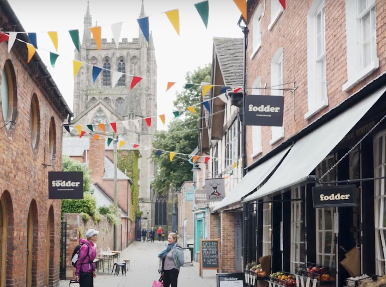 Hereford's Church Street a cobbled street with colourful bunting strung across it. Hereford Cathedral can be seen at the end of the street.