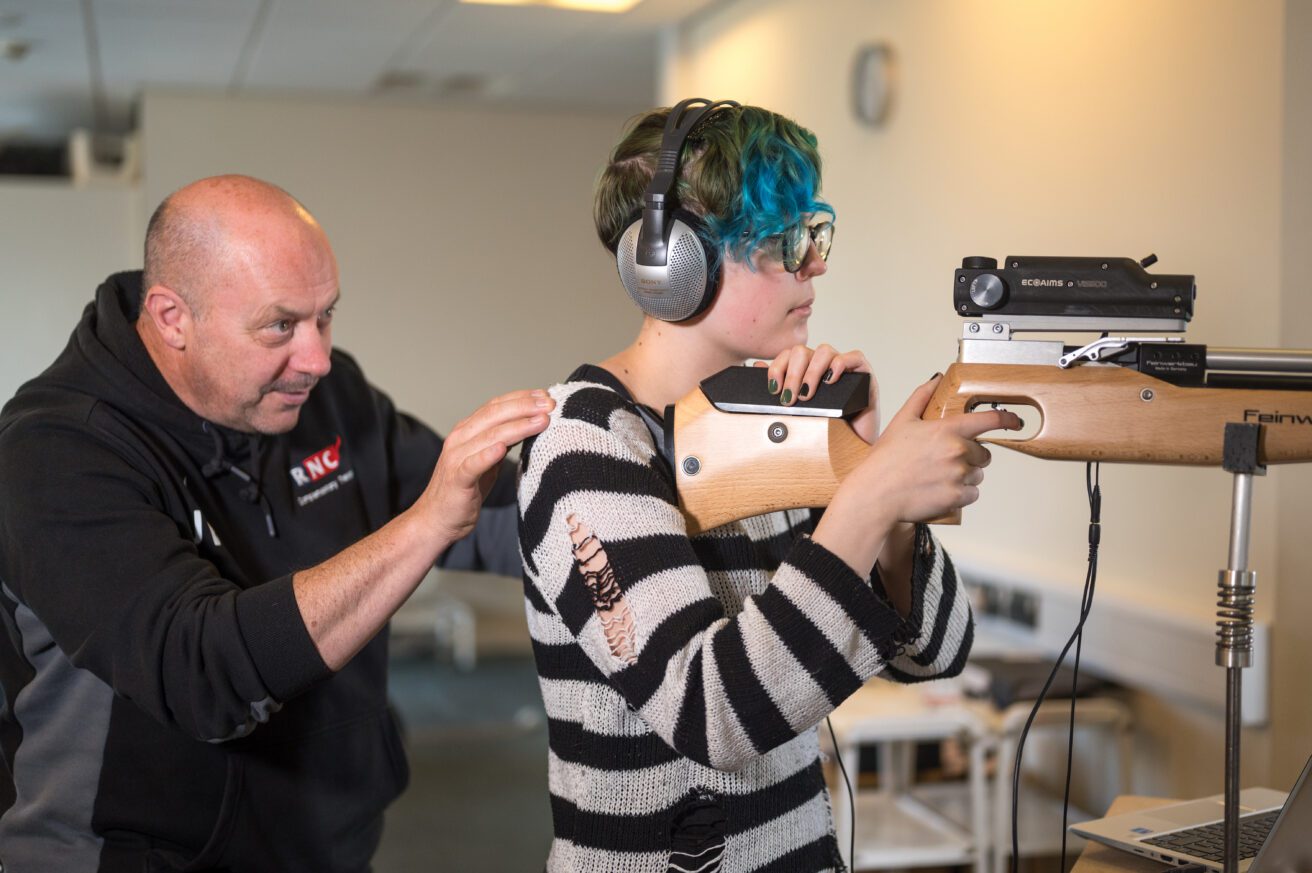 An acoustic shooting coach guiding a student who is wearing headphone and is about to shoot at the target