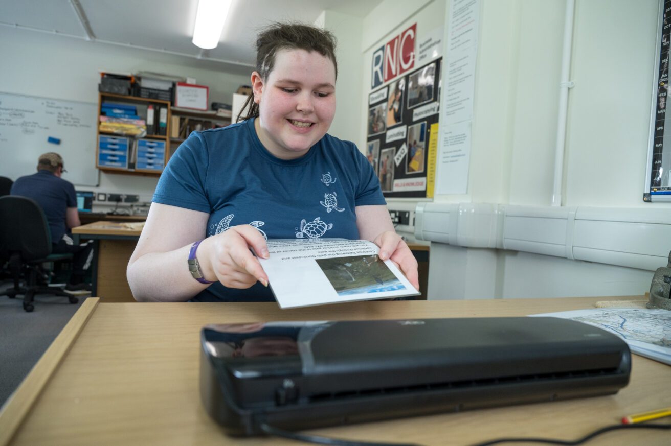 A student in the working office about to load a document into the laminating machine