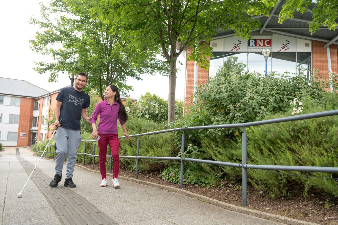two people walking together outside - one is using a cane