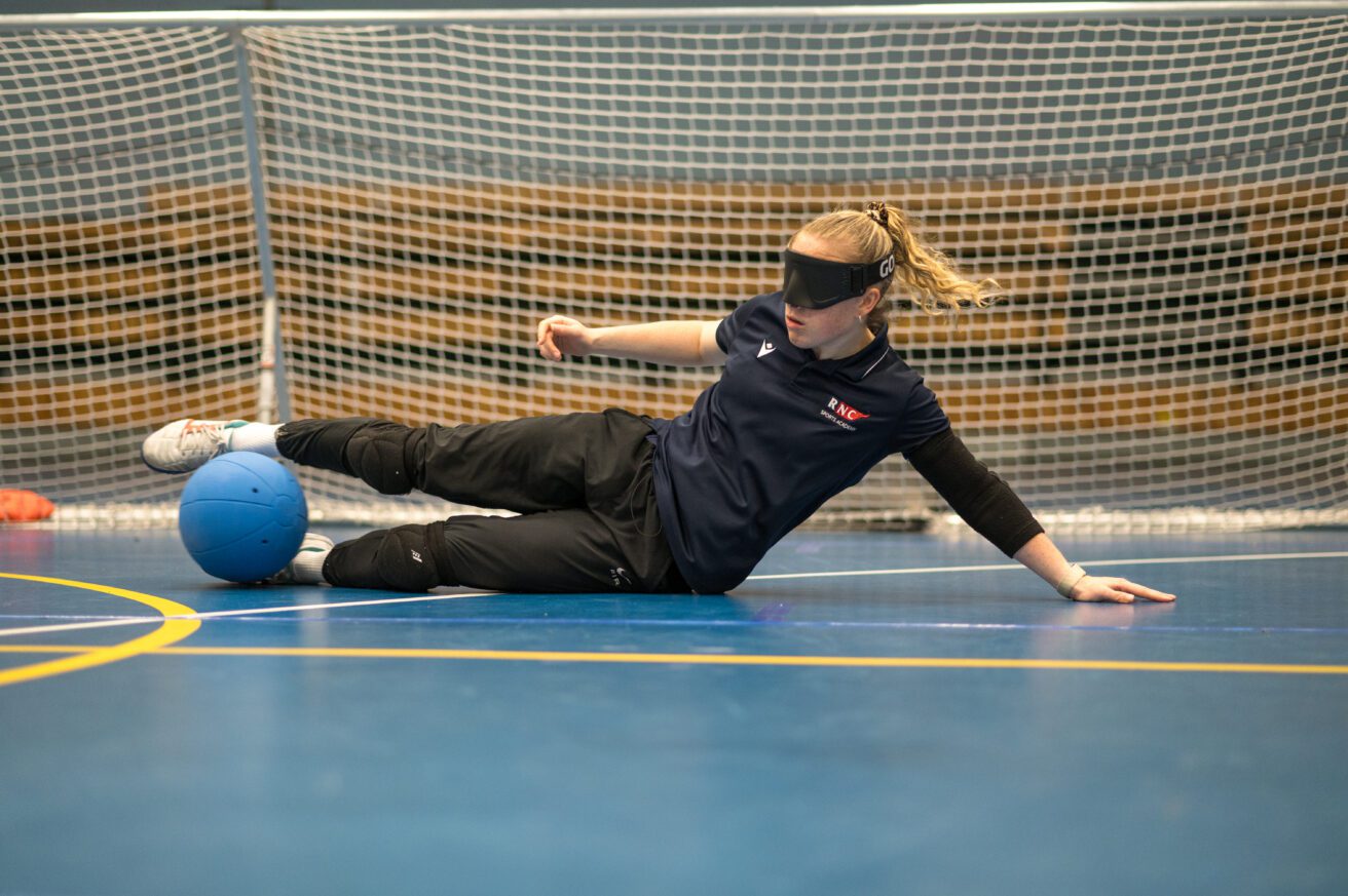 A goalball player lying in front of goal just about to trap an oncoming ball with her feet