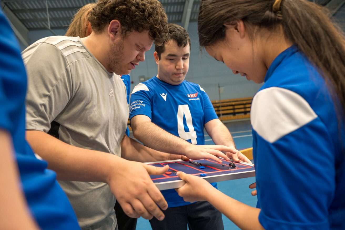 3 students congregate around a tactile board where they can plan their strategy for a game of goalball