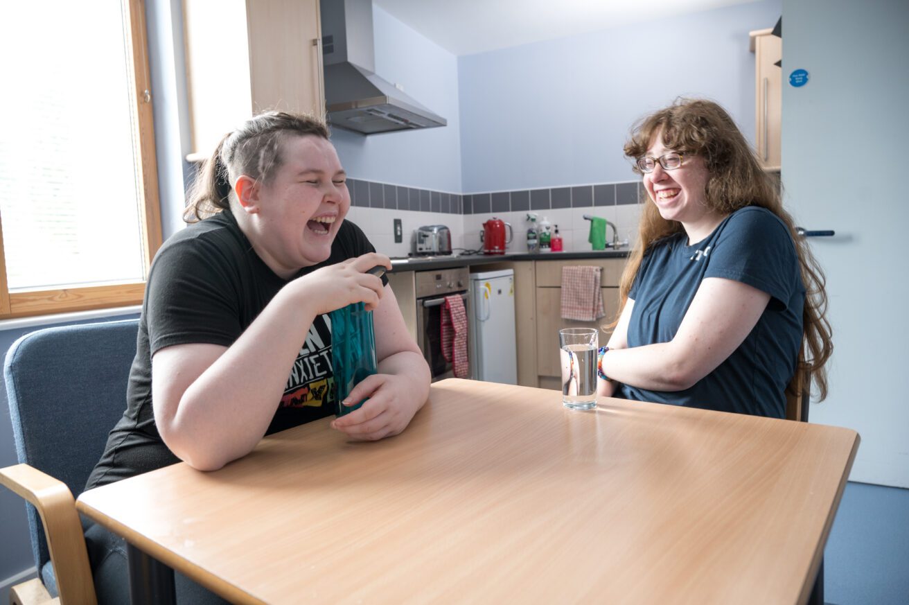Two students sitting across a kitchen both laughing