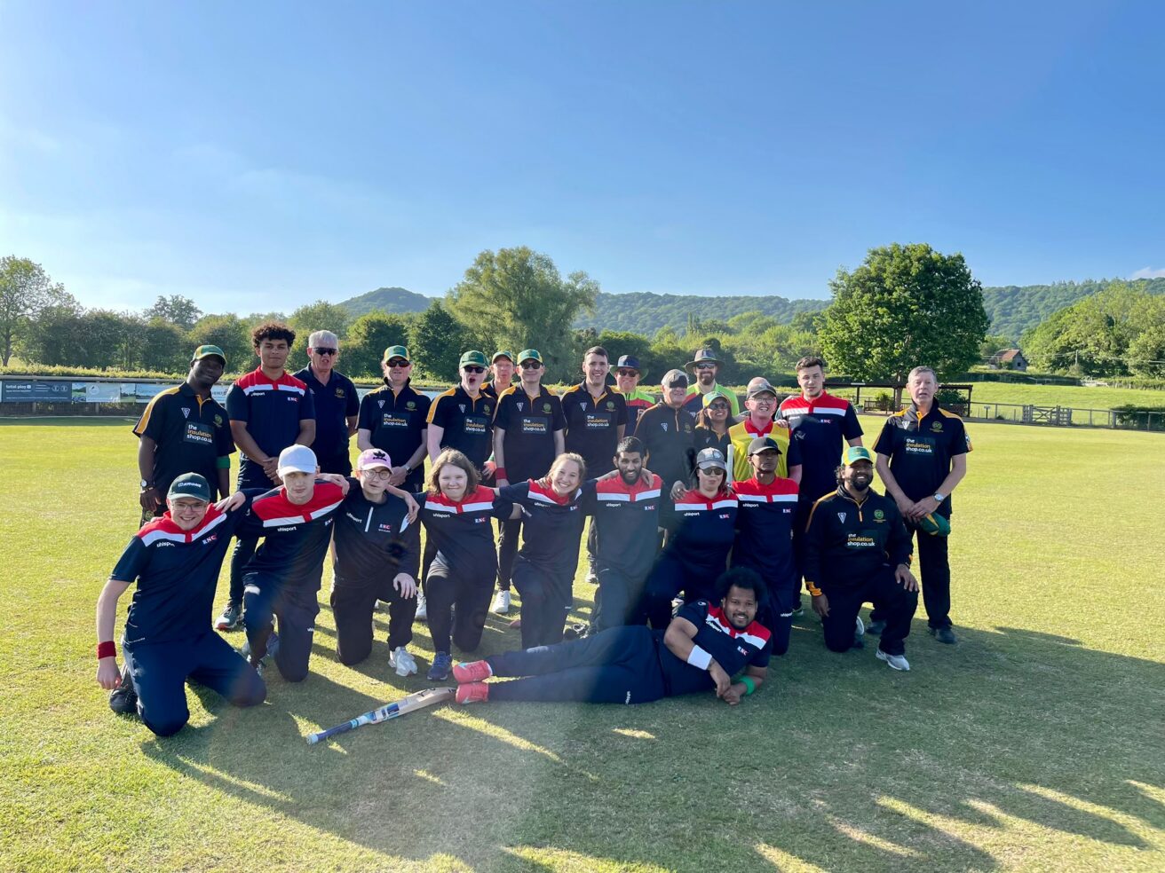A large group of players together on a cricket ground smiling for a team photo in the sunshine