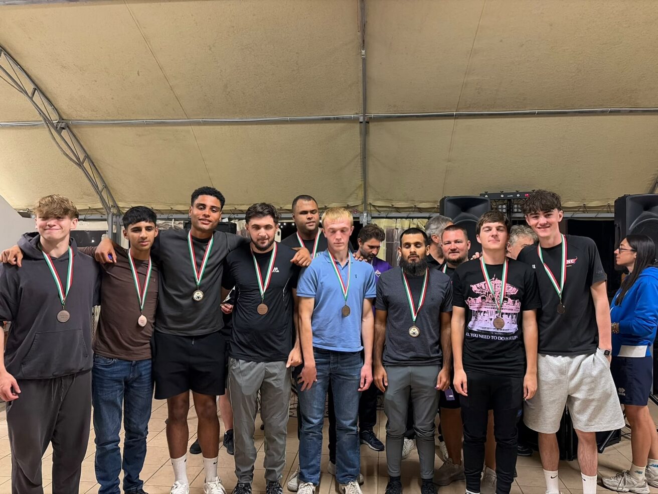 A group of ten male blind football team members and coaches posing together indoors, each wearing a medal on a ribbon around their neck.